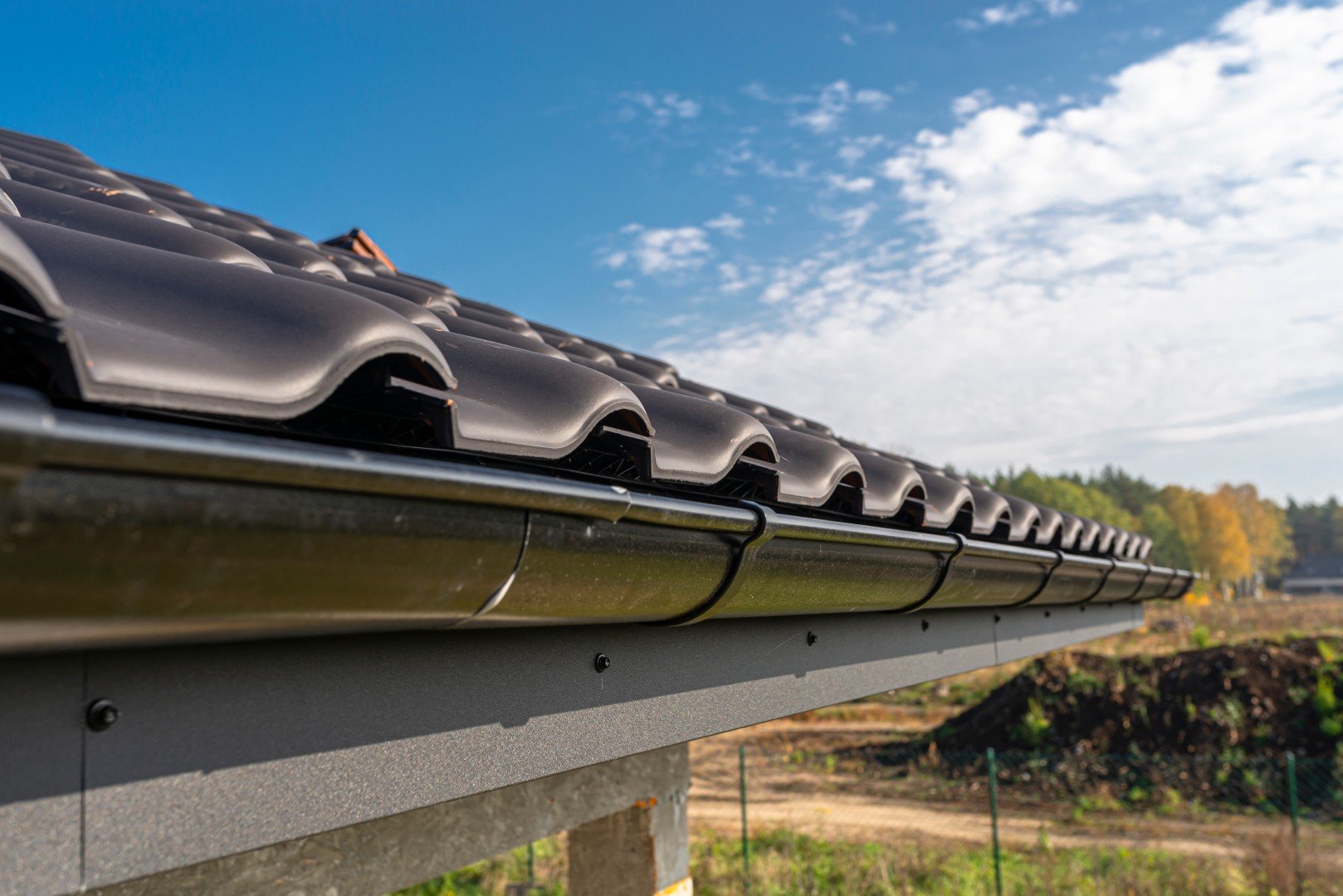 Close view of a black metal gutter and dark roof tiles under a blue sky