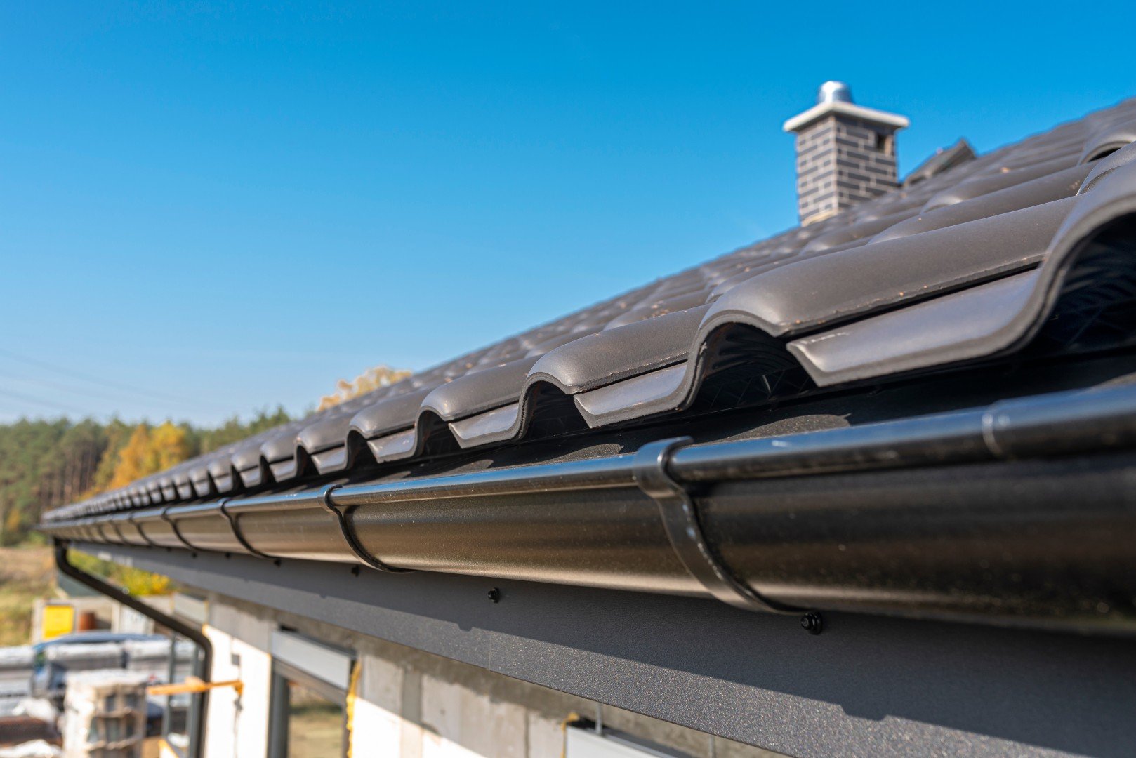 Black metal gutter along a dark tiled roof with a brick chimney